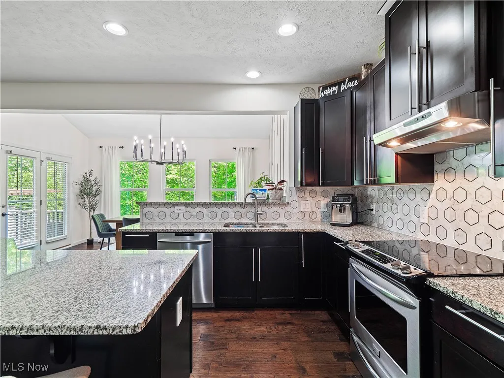 Kitchen featuring appliances with stainless steel finishes, under cabinet range hood, light stone counters, a peninsula, and recessed lighting