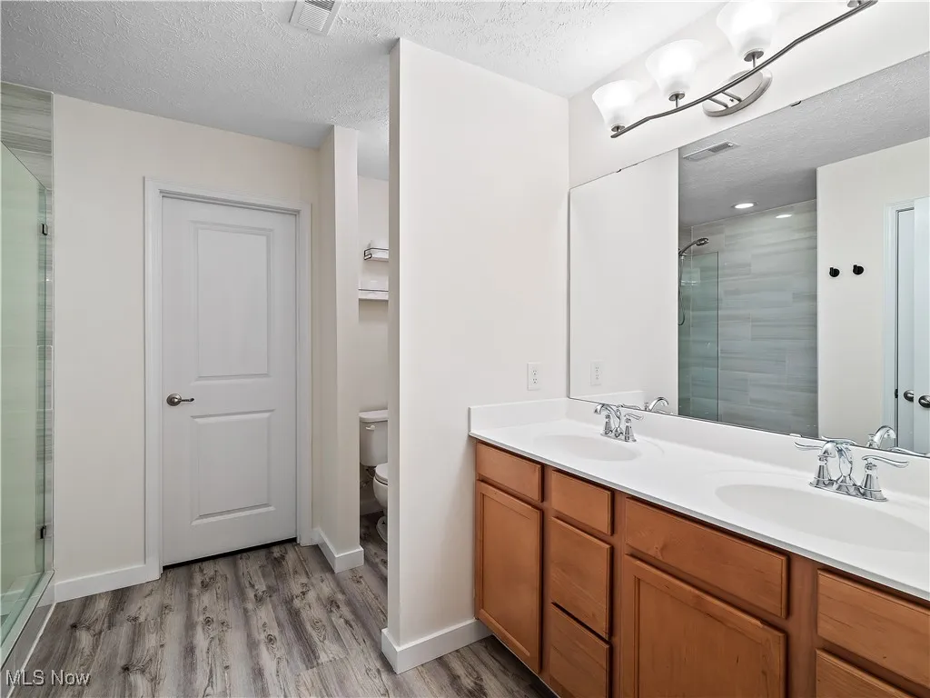 Full bath featuring an enclosed shower, double vanity, wood finished floors, and a textured ceiling