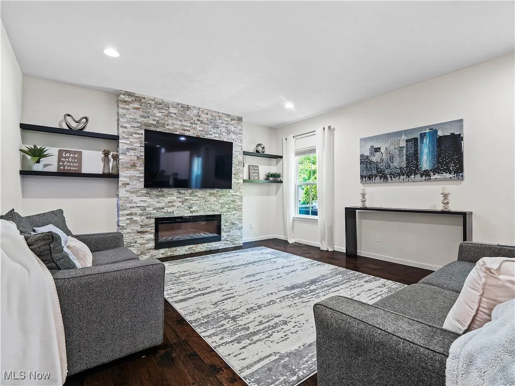 Living room with wood finished floors, a stone fireplace, and recessed lighting