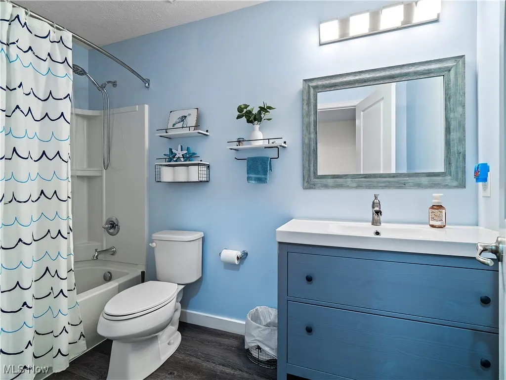 Full bath with vanity, shower / tub combo with curtain, wood finished floors, and a textured ceiling