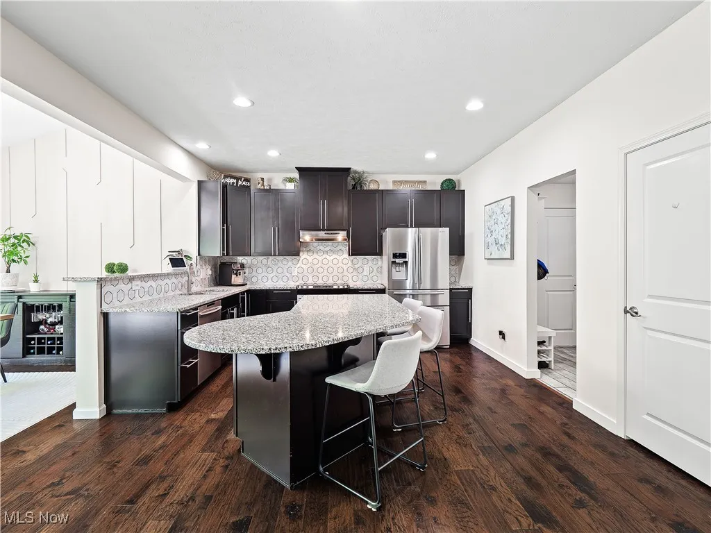 Kitchen with appliances with stainless steel finishes, under cabinet range hood, a kitchen breakfast bar, a center island, and tasteful backsplash