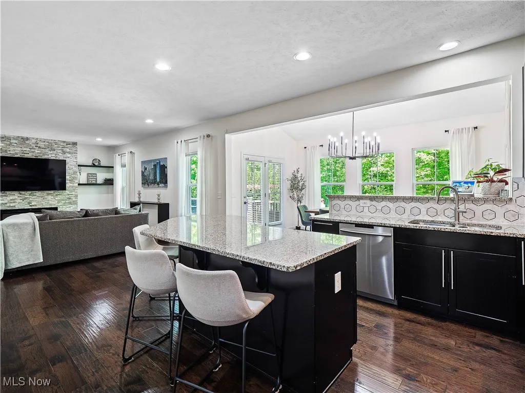 Kitchen featuring stainless steel dishwasher, a kitchen bar, light stone countertops, a kitchen island, and dark wood-style floors