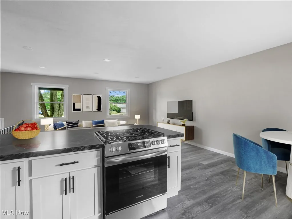 Kitchen featuring stainless steel gas range, open floor plan, dark countertops, dark wood-style flooring, and recessed lighting