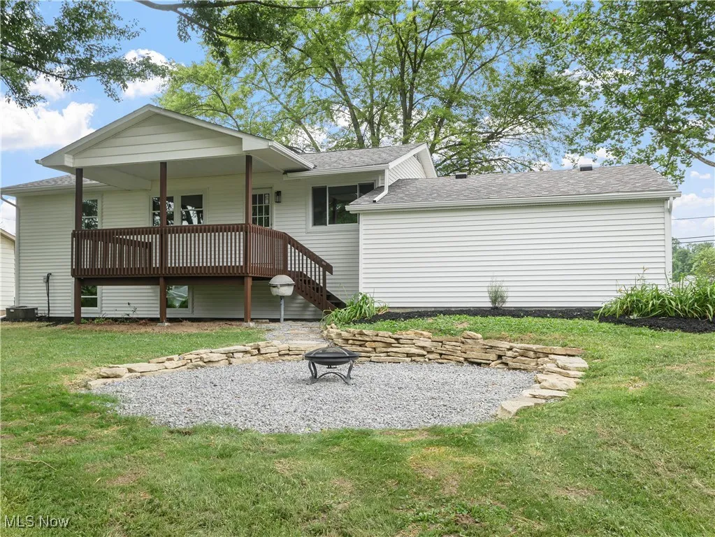 Rear view of property with a fire pit, a lawn, a deck, and a shingled roof