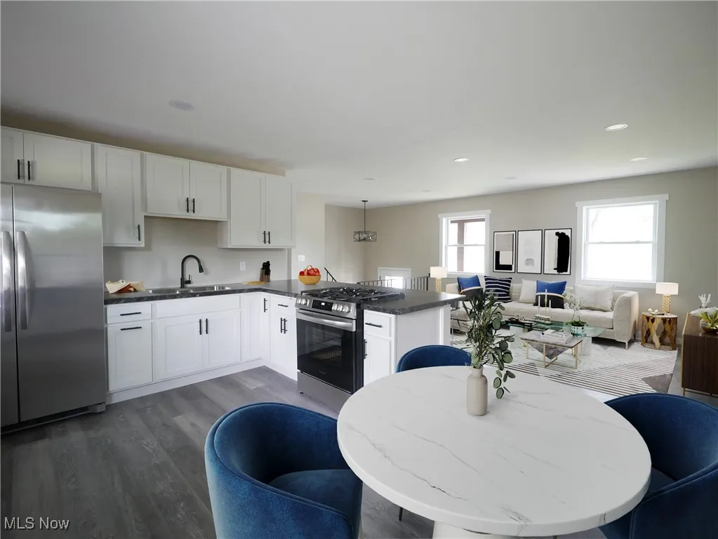 Kitchen with stainless steel appliances, a peninsula, wood finished floors, open floor plan, and white cabinetry