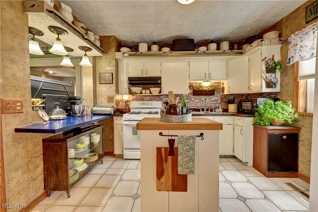 Kitchen with white gas range, under cabinet range hood, white cabinetry, a kitchen island, and light tile patterned flooring