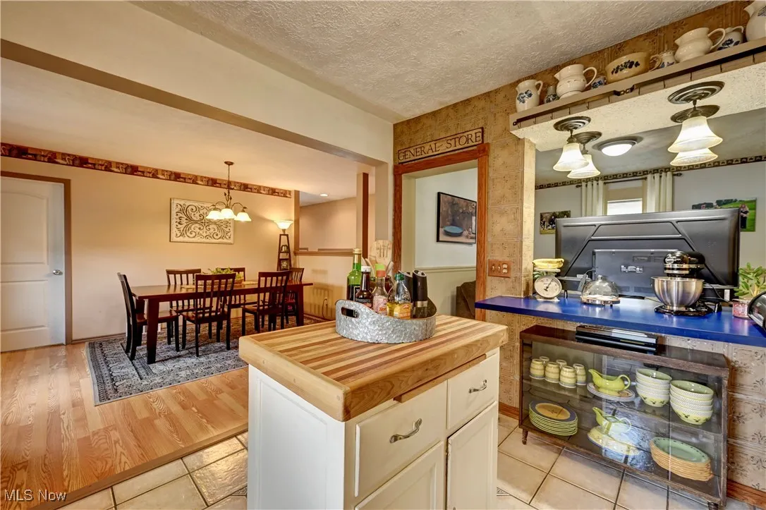 Kitchen with butcher block countertops, white cabinets, a textured ceiling, hanging light fixtures, and light tile patterned floors