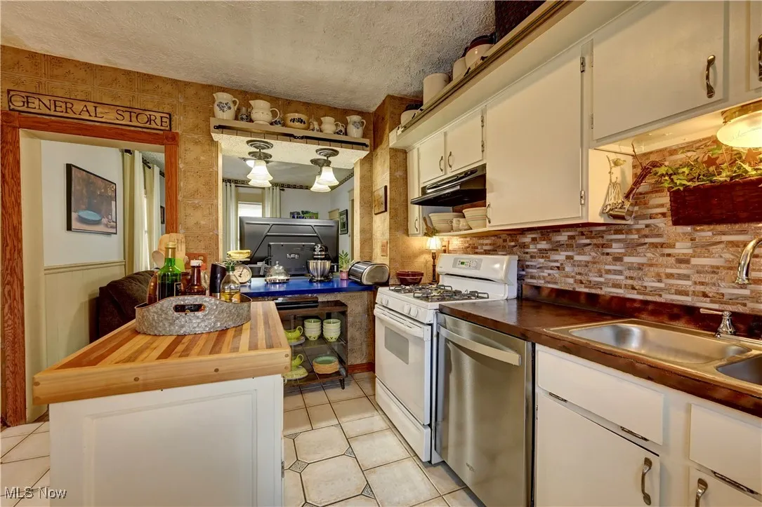 Kitchen featuring white gas range oven, dishwasher, wood counters, light tile patterned floors, and a textured ceiling