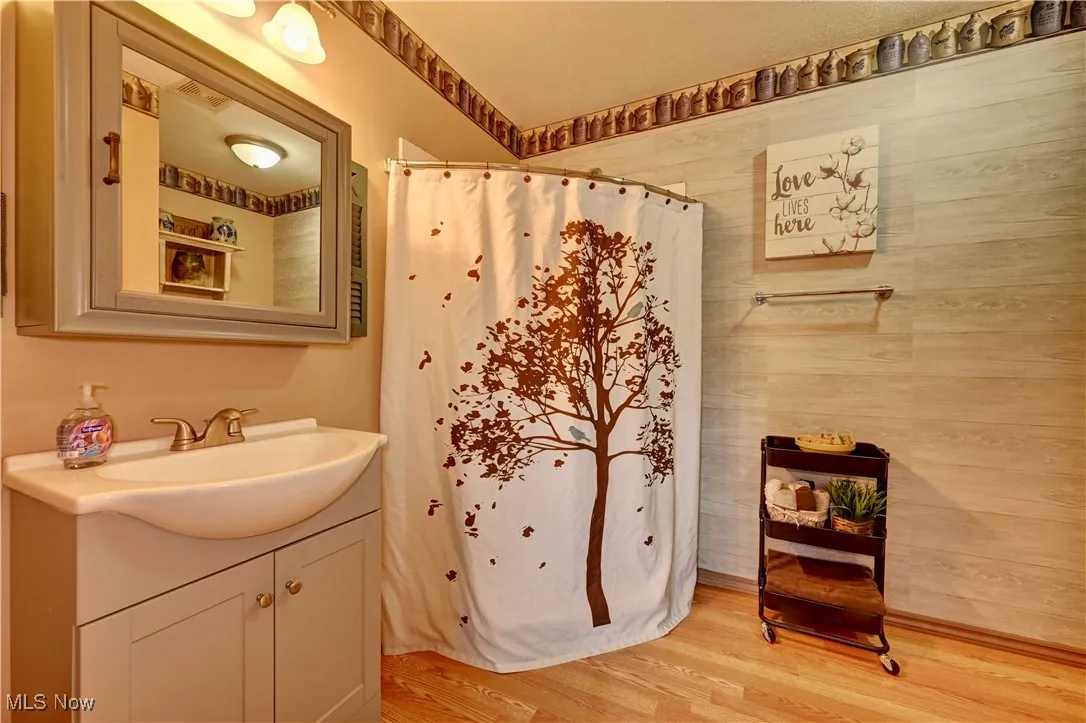 Full bath with vanity, wood finished floors, a shower with shower curtain, and wood walls