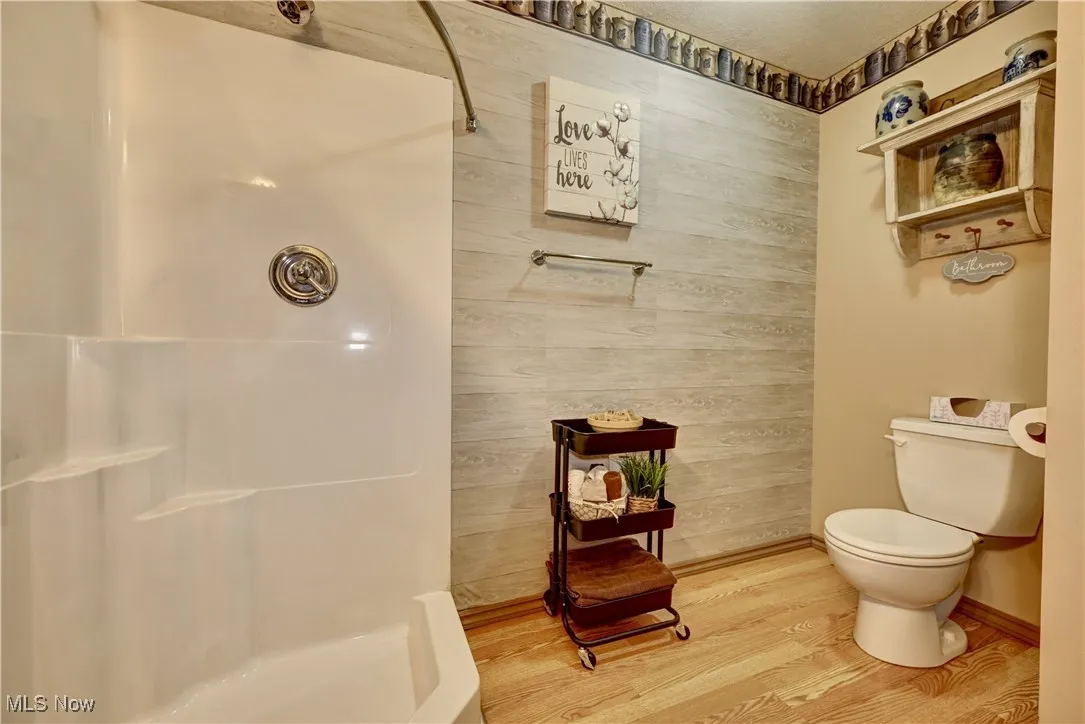 Full bath with a shower, wood finished floors, and wooden walls