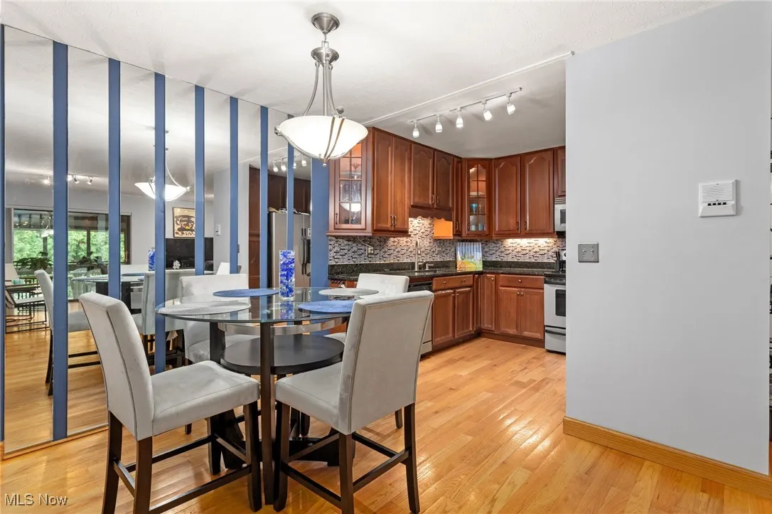 Kitchen featuring stainless steel appliances, dark countertops, backsplash, glass insert cabinets, and light wood-style flooring