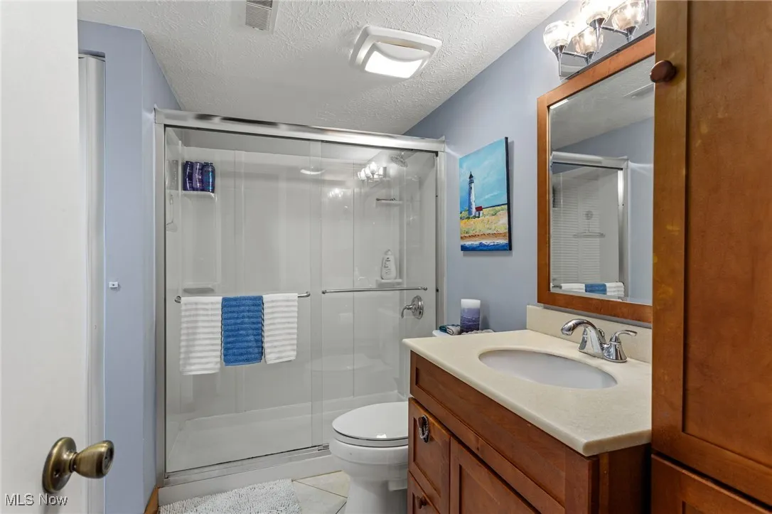 Bathroom featuring a stall shower, vanity, tile patterned floors, and a textured ceiling