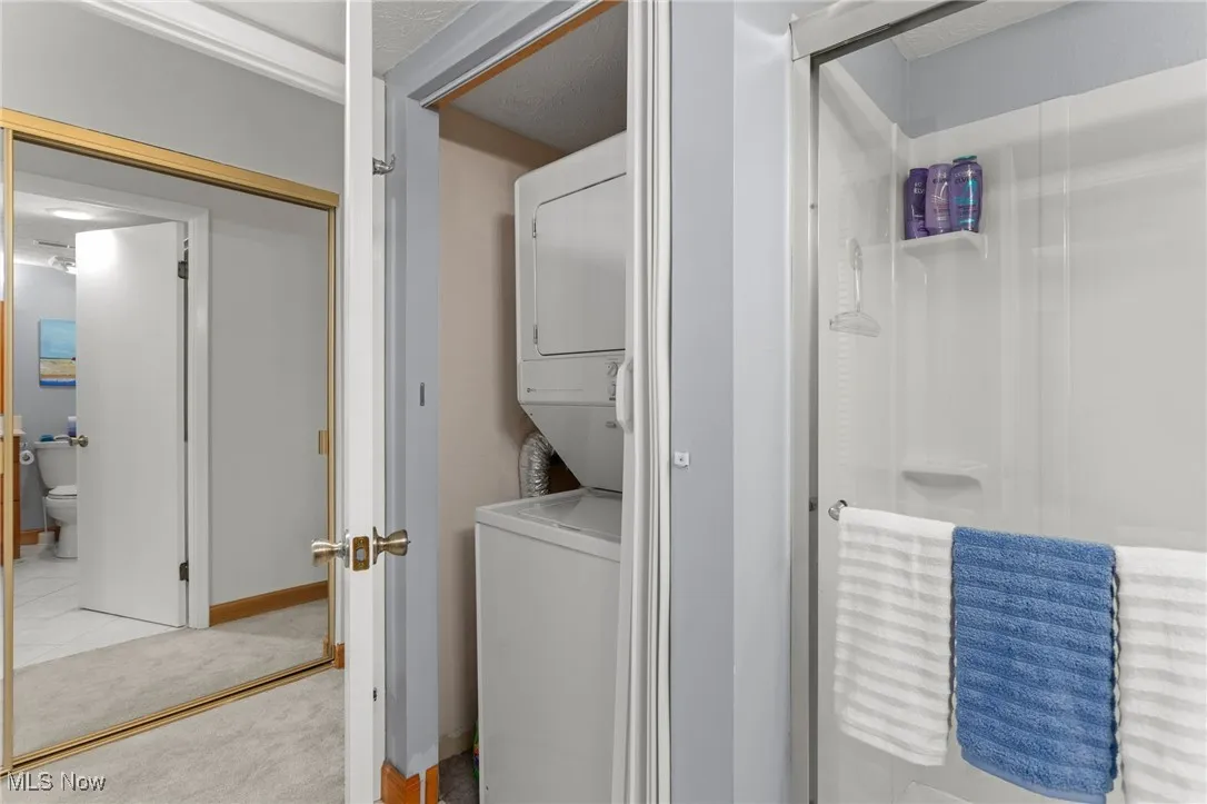Laundry room with stacked washer / drying machine and light carpet