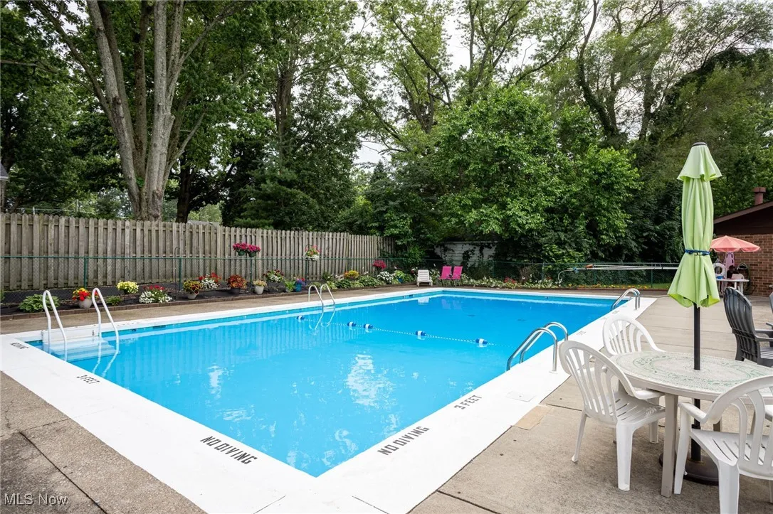 Community pool with a fenced backyard, view of scattered trees, and a patio area