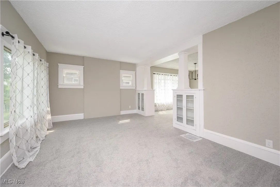 Unfurnished living room featuring healthy amount of natural light, carpet floors, ornate columns, and a textured ceiling