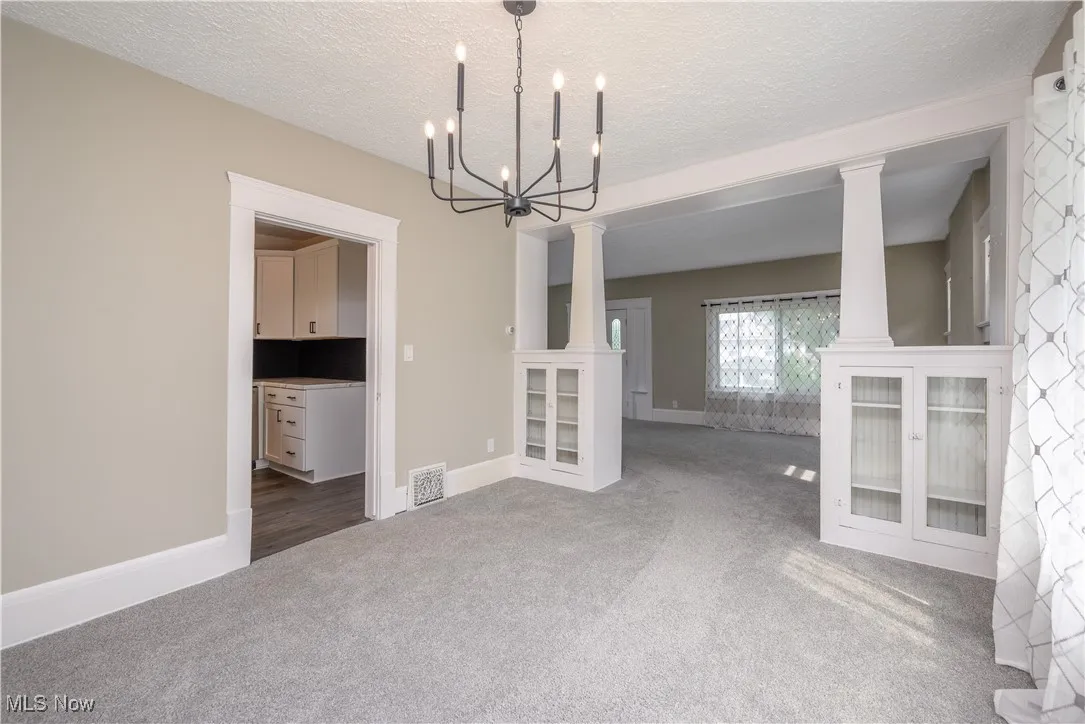 Unfurnished dining area featuring carpet, a chandelier, ornate columns, and a textured ceiling