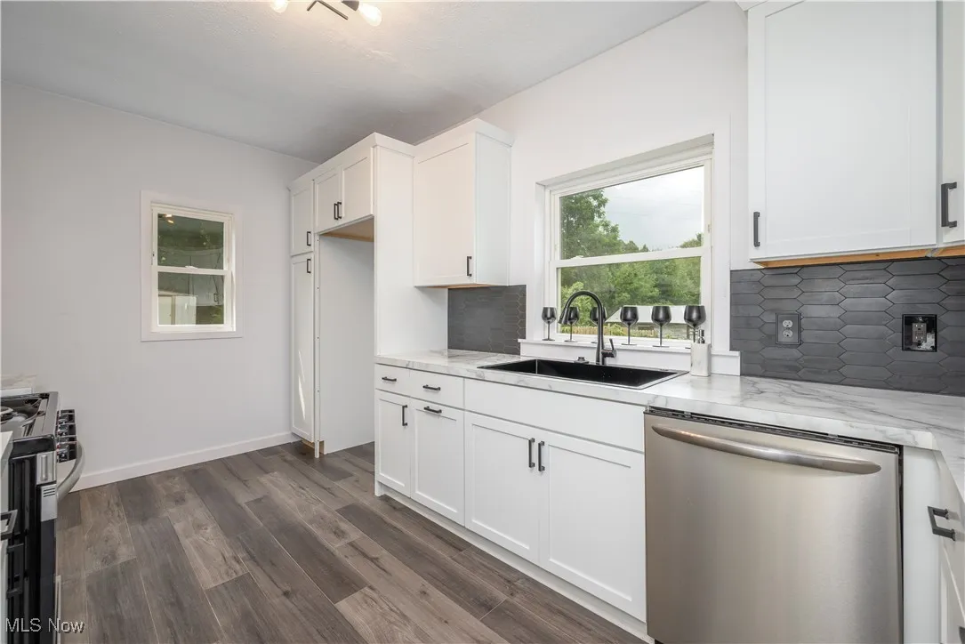 Kitchen featuring appliances with stainless steel finishes, dark wood-style floors, decorative backsplash, light stone countertops, and white cabinetry