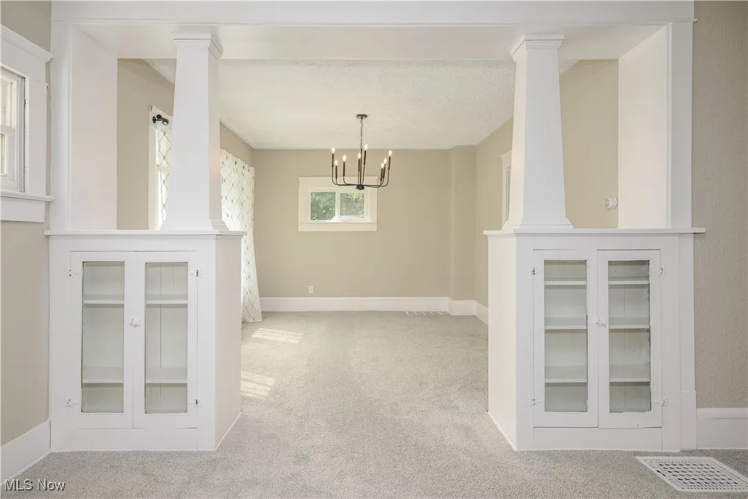 Unfurnished dining area featuring carpet floors, a chandelier, and ornate columns
