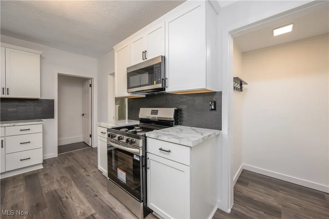 Kitchen with appliances with stainless steel finishes, dark wood finished floors, backsplash, light countertops, and a textured ceiling