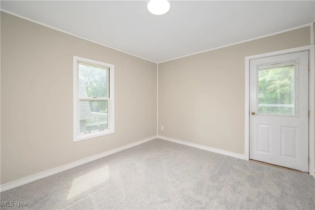 Carpeted empty room with healthy amount of natural light and ornamental molding