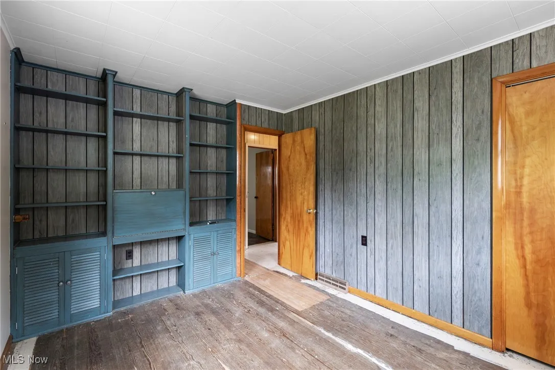 Unfurnished bedroom with wood finished floors, ornamental molding, and wooden walls