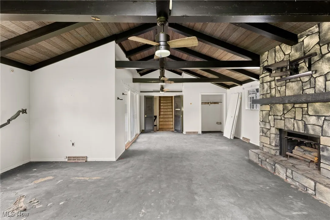 Unfurnished living room featuring a ceiling fan, a stone fireplace, and wooden ceiling