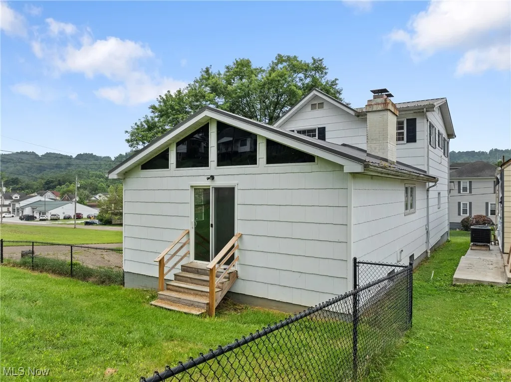 Back of property with entry steps, a fenced backyard, and a chimney