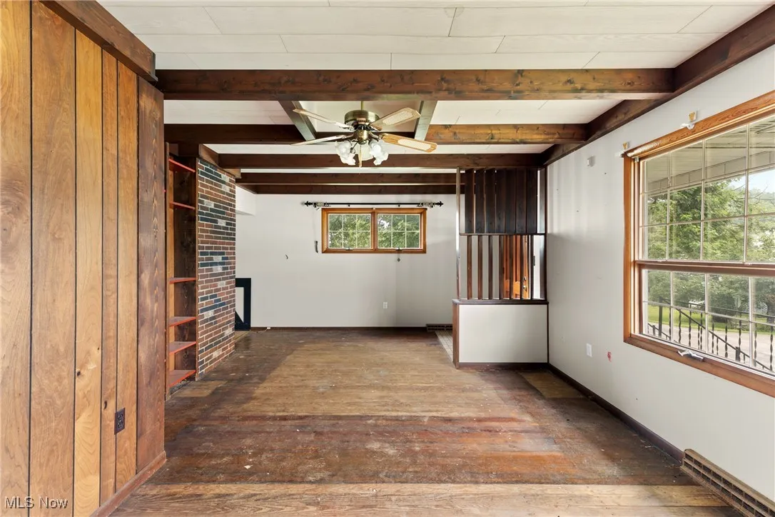 Unfurnished living room with a baseboard heating unit, beam ceiling, a ceiling fan, and wood-type flooring