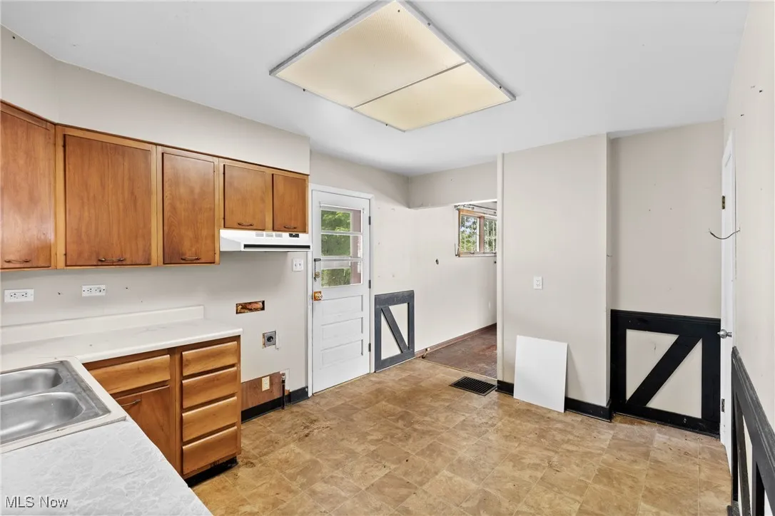 Kitchen featuring brown cabinets, under cabinet range hood, and light countertops