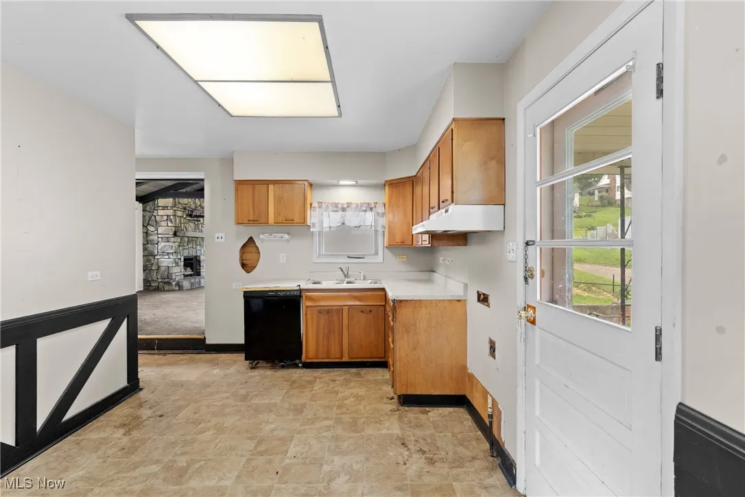 Kitchen featuring dishwasher, under cabinet range hood, light countertops, brown cabinetry, and healthy amount of natural light