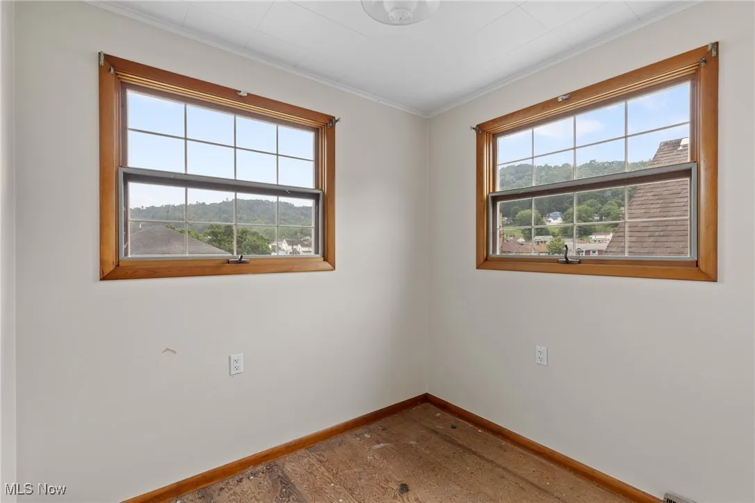 Empty room featuring plenty of natural light, wood finished floors, and ornamental molding