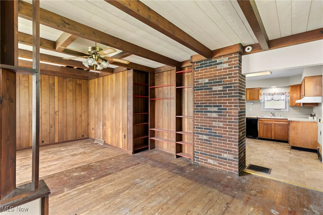 Unfurnished living room featuring beamed ceiling, wood walls, ceiling fan, and light wood-style flooring