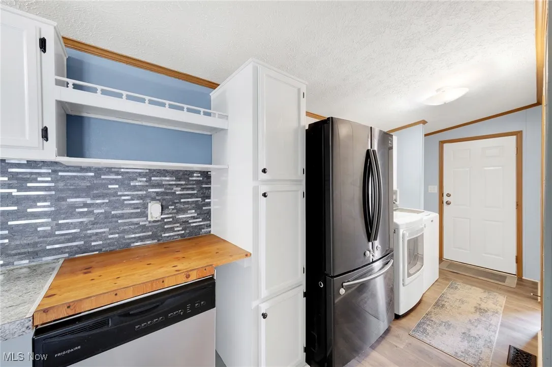 Kitchen featuring stainless steel appliances, washer and clothes dryer, backsplash, white cabinets, and light wood-type flooring