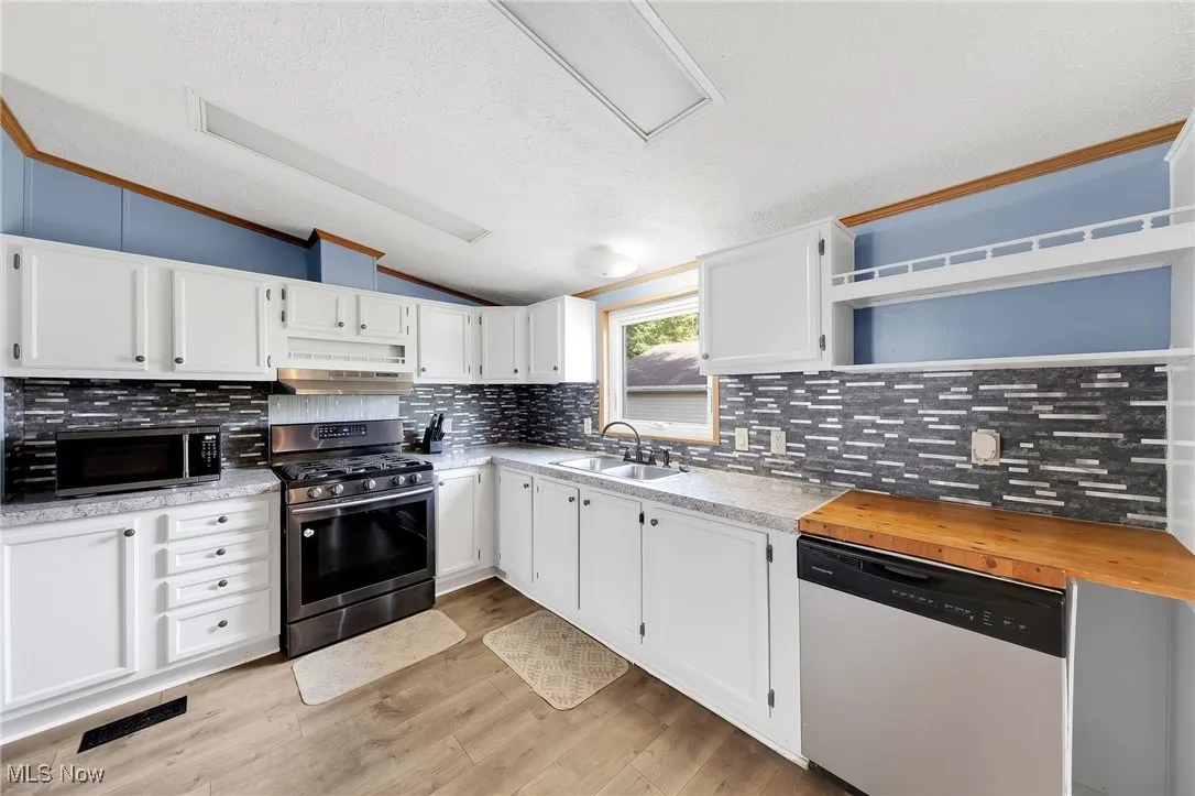 Kitchen with stainless steel appliances, lofted ceiling, under cabinet range hood, a textured ceiling, and white cabinetry