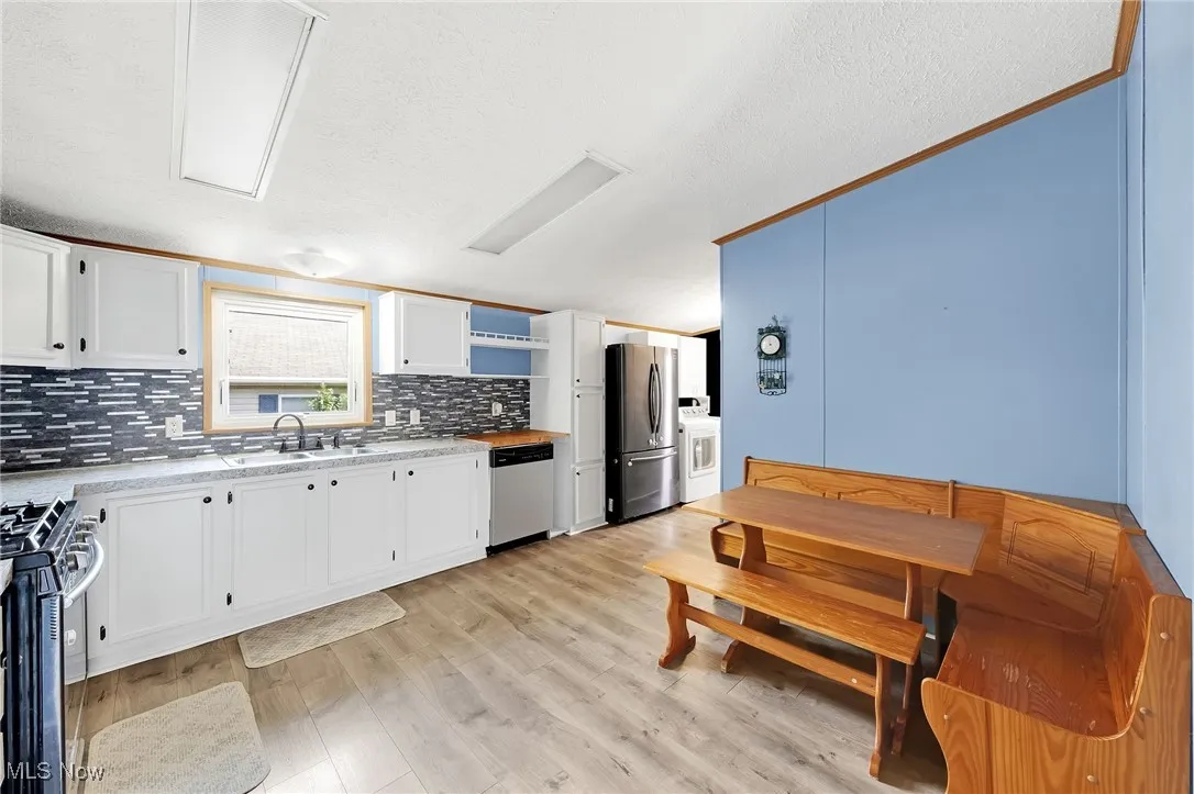 Kitchen with stainless steel appliances, separate washer and dryer, backsplash, light countertops, and white cabinetry