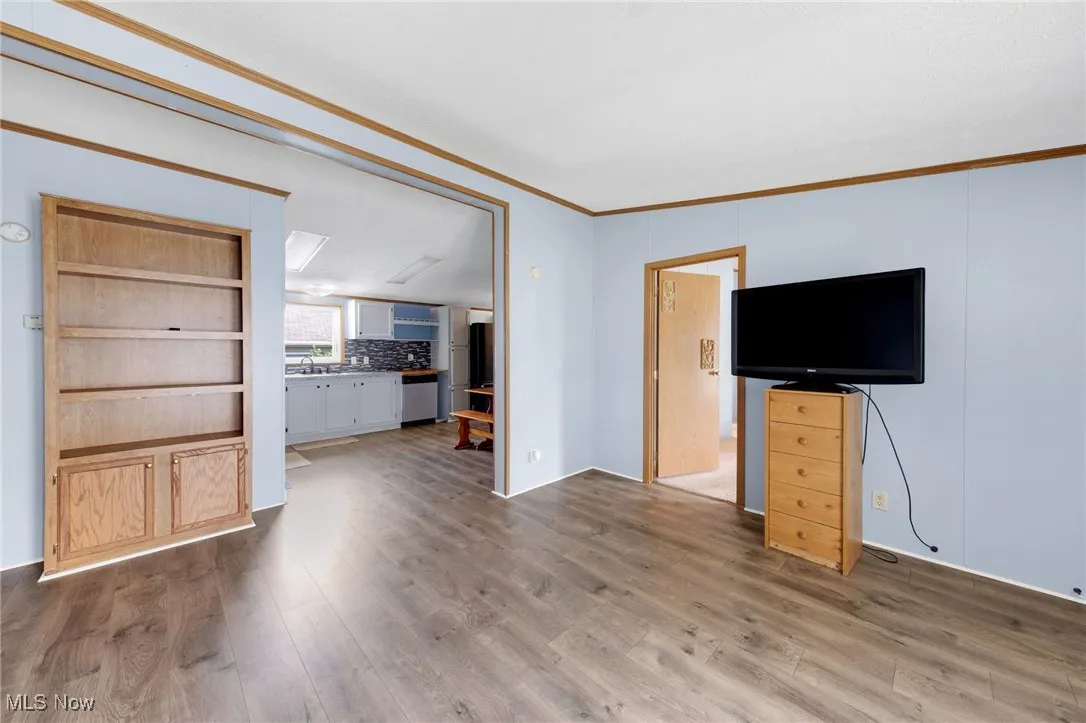Unfurnished living room with wood finished floors and crown molding