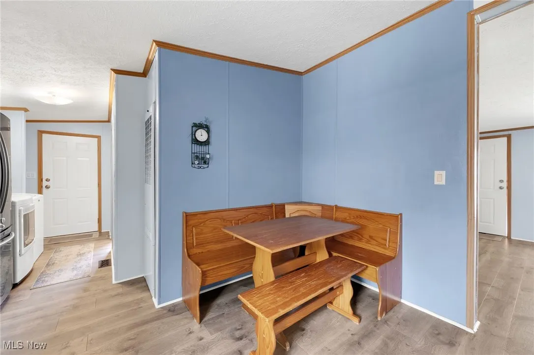 Dining area with crown molding, light wood-style flooring, and a textured ceiling
