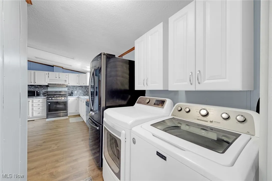 Laundry room featuring separate washer and dryer, light wood-type flooring, a textured ceiling, and cabinet space