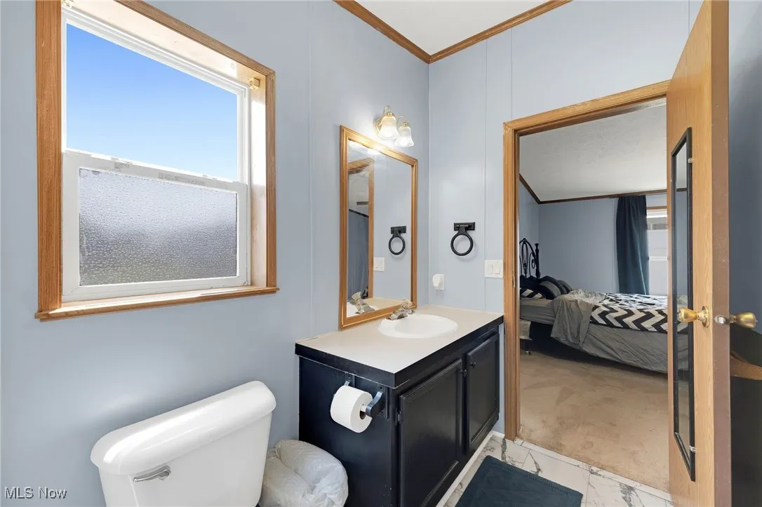 Ensuite bathroom featuring crown molding, vanity, and marble look tiles