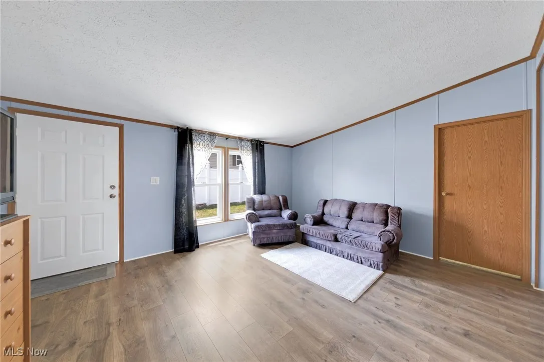 Living area with crown molding, a textured ceiling, vaulted ceiling, and wood finished floors
