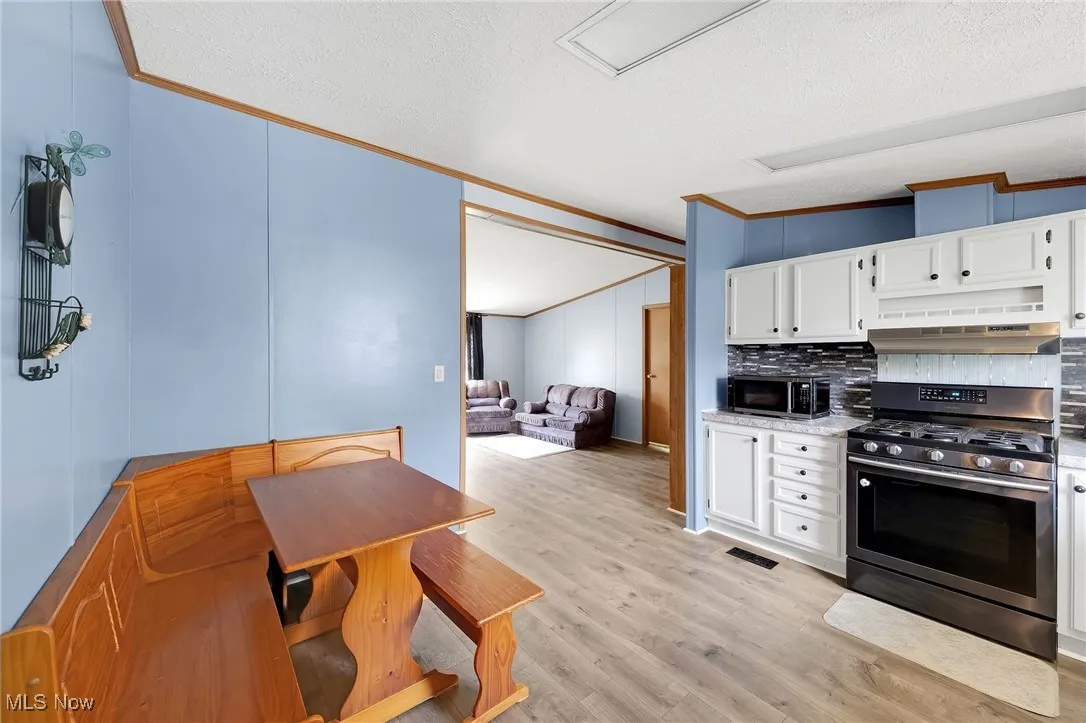 Kitchen featuring appliances with stainless steel finishes, crown molding, a textured ceiling, tasteful backsplash, and light wood-style flooring