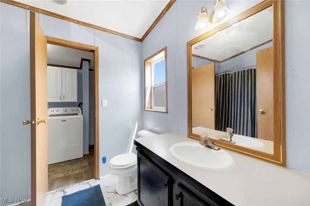 Full bath with washer / dryer, crown molding, vanity, marble look tile flooring, and curtained shower