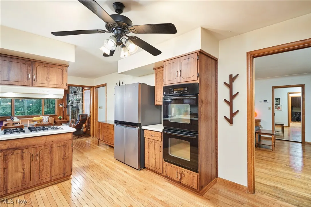 Kitchen with freestanding refrigerator, under cabinet range hood, light wood-style floors, ceiling fan, and light countertops