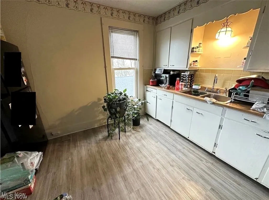 Kitchen with light wood-style flooring, white cabinets, backsplash, and open shelves