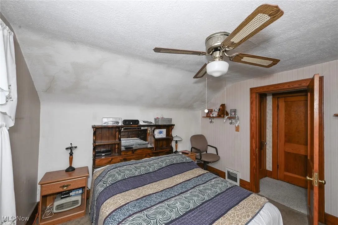 Carpeted bedroom featuring a textured ceiling, a ceiling fan, and lofted ceiling