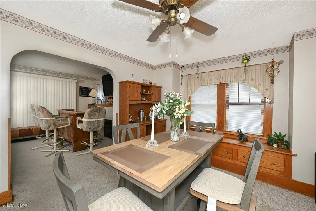Carpeted dining space featuring ceiling fan, a textured ceiling, and arched walkways