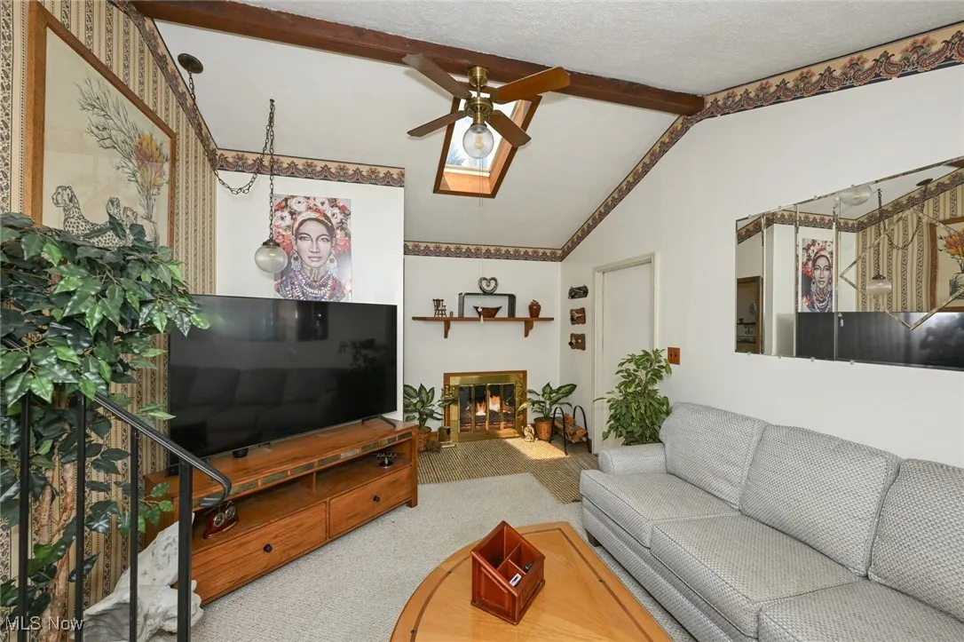 Carpeted living room featuring ceiling fan and a glass covered fireplace