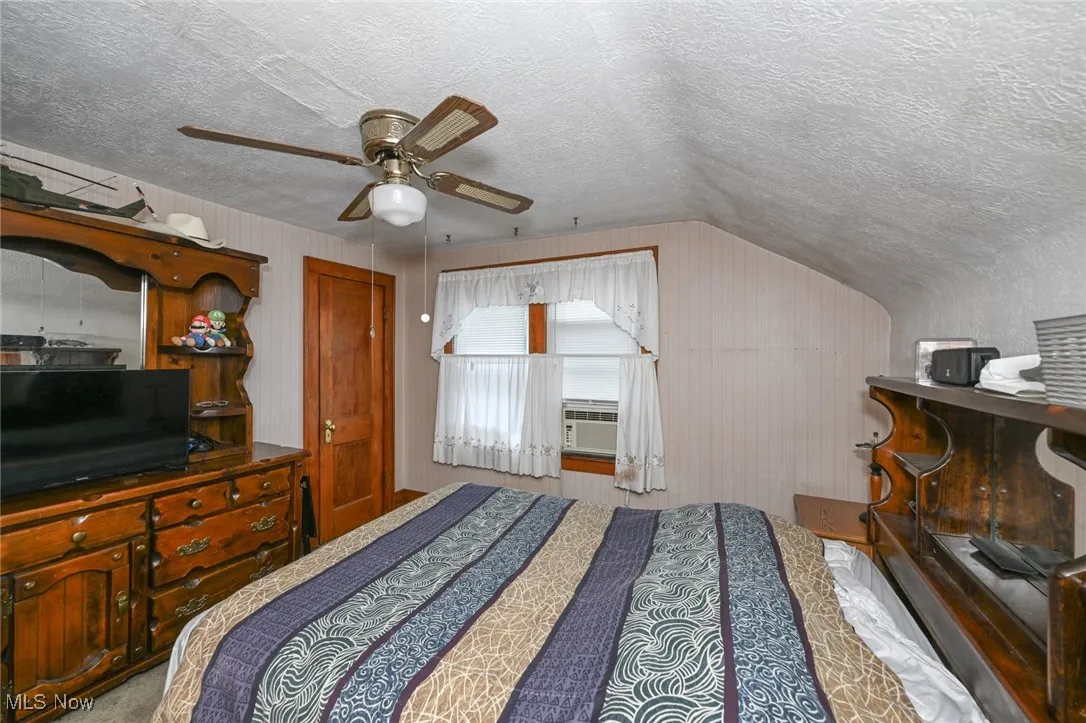 Bedroom with vaulted ceiling, a textured ceiling, and ceiling fan