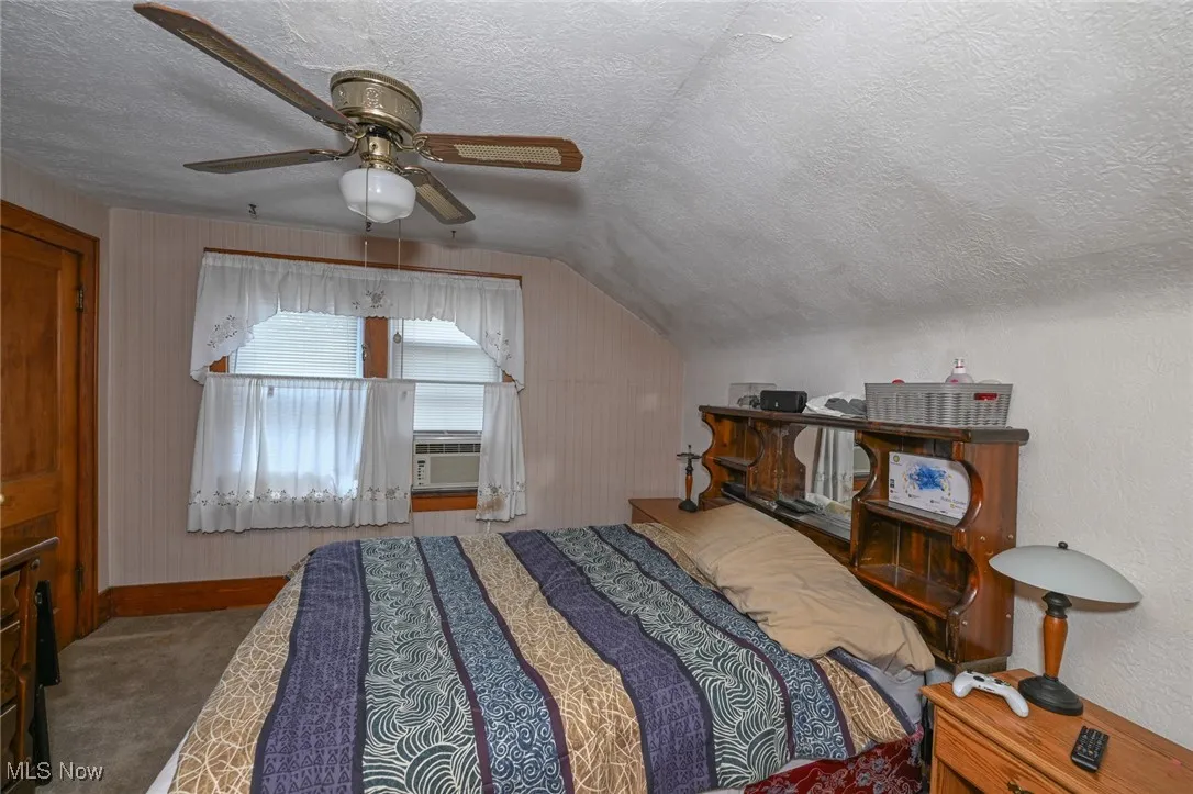 Carpeted bedroom with a textured ceiling, lofted ceiling, a ceiling fan, and cooling unit