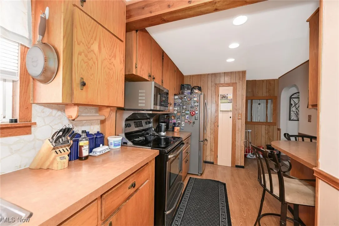 Kitchen with stainless steel appliances, light countertops, backsplash, light wood finished floors, and wood walls